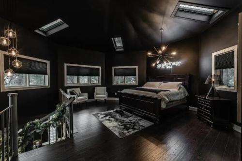 A modern bedroom with dark walls, a large bed, stylish lighting, and windows, creating a cozy atmosphere.