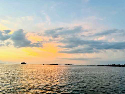 A serene sunset over calm waters, with soft clouds and distant islands silhouetted against a colorful sky.