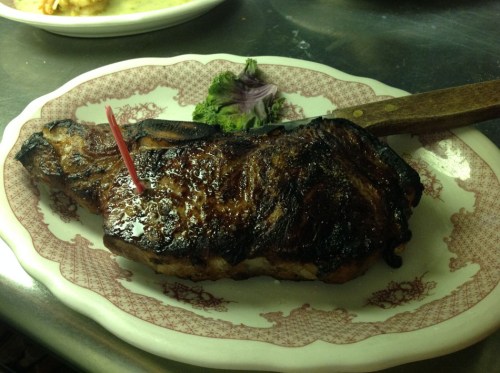 A grilled steak on a decorative plate, garnished with a small piece of broccoli and a toothpick.