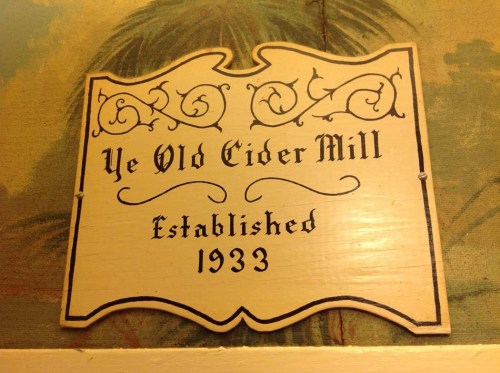 Sign for "Ye Old Cider Mill," established in 1933, featuring decorative lettering on a wooden background.