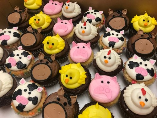 A variety of colorful cupcakes decorated as farm animals, including pigs, cows, chickens, and horses.