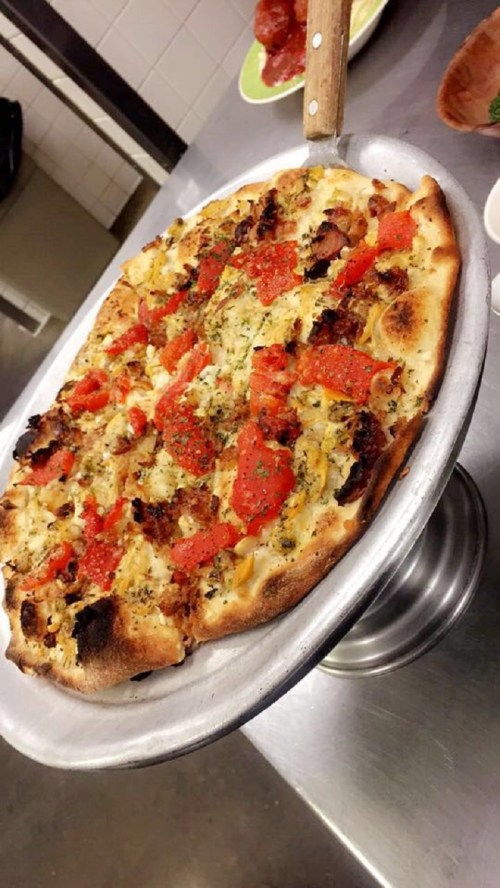 A freshly baked pizza on a metal stand, topped with pepperoni, herbs, and a golden crust.