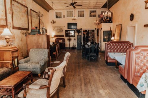 Cozy restaurant interior with vintage furniture, including armchairs and booths, warm lighting, and rustic decor.