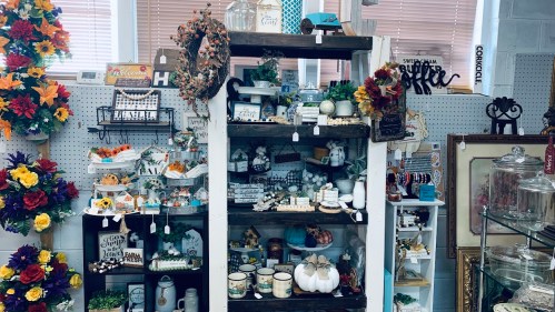 A wooden display shelf filled with various decorative items, including plants, signs, and seasonal decor.