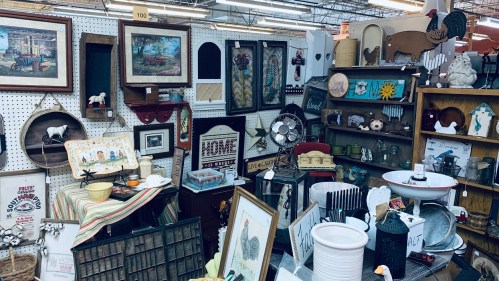A vibrant display of vintage decor and antiques, including framed art, kitchenware, and rustic items in a market setting.