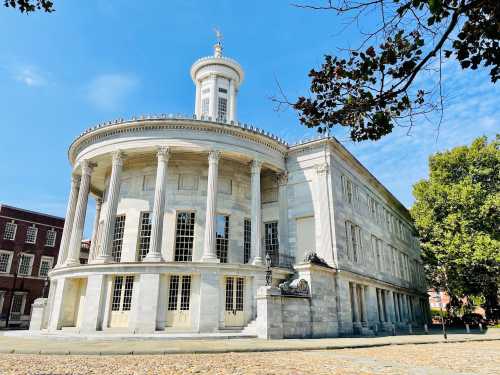 A grand, circular building with columns and a dome, surrounded by trees and a clear blue sky.