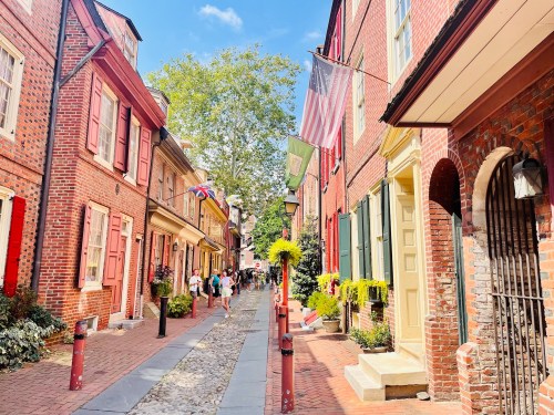 Charming cobblestone street lined with colorful historic buildings and flags, bustling with people on a sunny day.