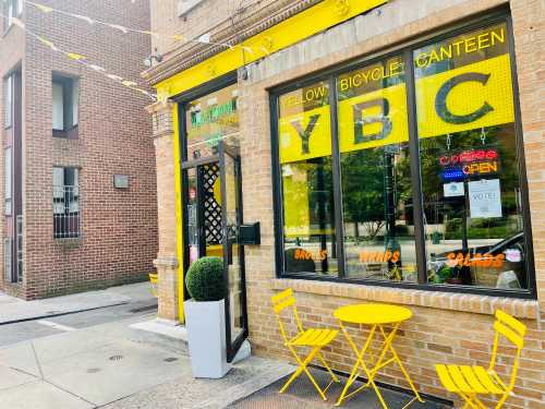 Bright yellow café entrance with outdoor seating, featuring "YBC" signage and a welcoming atmosphere.