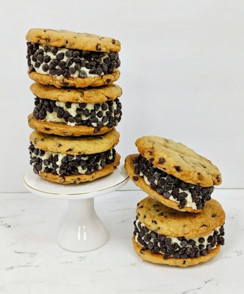 A stack of chocolate chip cookie ice cream sandwiches, coated with mini chocolate chips, on a white pedestal.