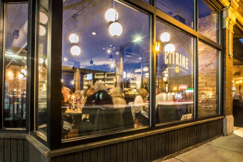 A cozy restaurant interior with warm lighting, visible through large windows, showcasing diners enjoying their meals.