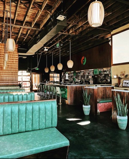 A stylish restaurant interior featuring green booths, a bar, and modern lighting in a warm, inviting atmosphere.