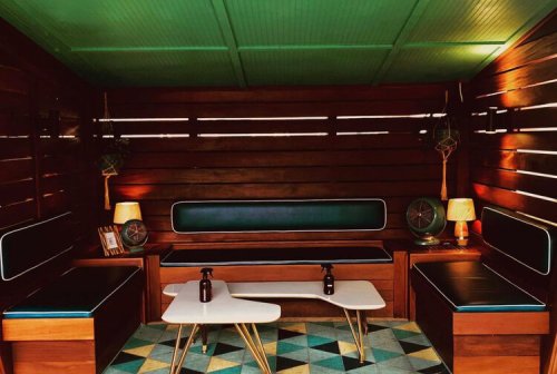 Cozy wooden lounge area with green ceiling, modern furniture, and geometric rug, featuring a coffee table and decorative lamps.