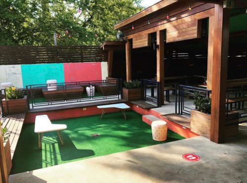 A cozy outdoor seating area with wooden structures, green grass, and colorful walls, perfect for relaxation.