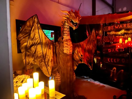 A large, golden dragon statue with outstretched wings stands in a dimly lit room decorated for Halloween.