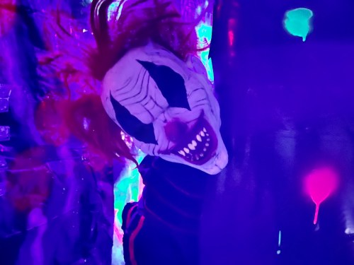A creepy clown mask with wild red hair, set against a colorful, abstract background.