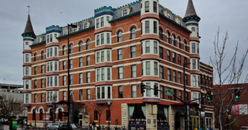 Historic brick building with turrets and decorative trim, featuring shops on the ground floor and a cloudy sky above.