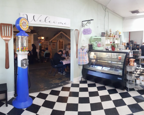 A cozy café entrance with a colorful gumball machine and a display case, featuring a checkered floor and welcoming decor.