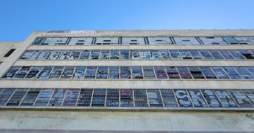 A tall, abandoned building with numerous windows covered in colorful graffiti against a clear blue sky.