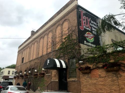 A brick building with a sign reading "Jax" and ivy climbing the walls, located in a neighborhood setting.