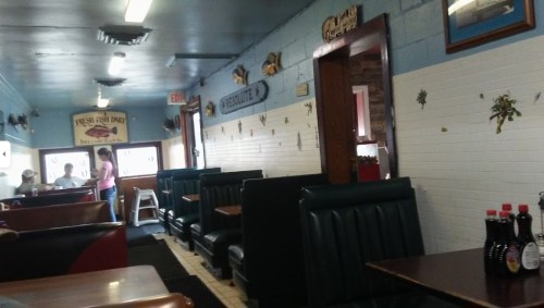 Interior of a casual diner with booths, a counter, and decor on the walls. A few customers are present.