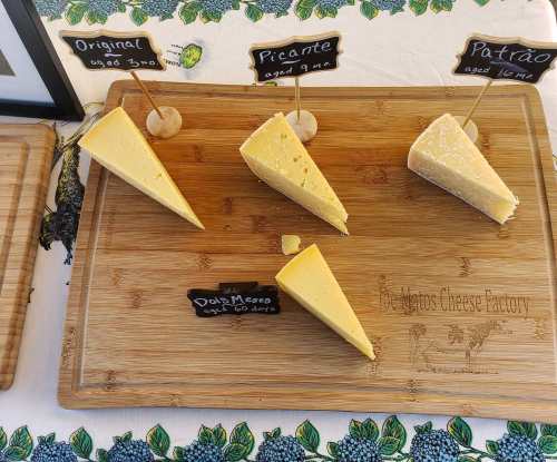 Four cheese samples displayed on a wooden board, labeled Original, Picante, and Patrão, with a decorative background.