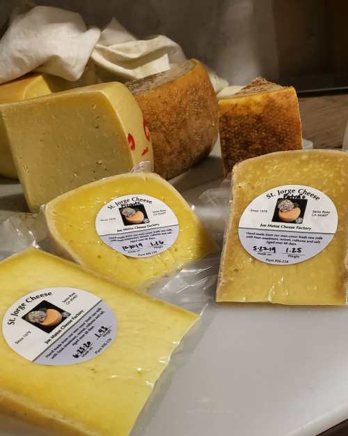 Assorted cheeses with labels on a cutting board, featuring various shapes and textures.