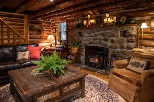 Cozy log cabin living room with a stone fireplace, comfortable seating, and warm lighting.