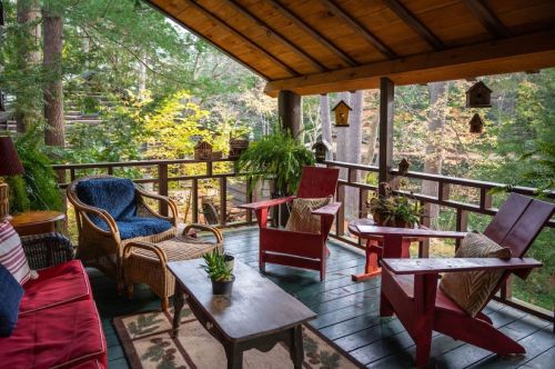 Cozy porch with red chairs, a wooden table, and lush greenery, surrounded by trees in a serene outdoor setting.