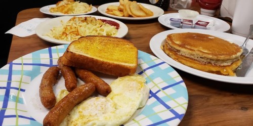 A breakfast spread featuring toast, sausages, eggs, pancakes, and hash browns on plates.