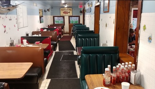 A cozy diner interior with green and brown booths, tables, and condiments on the counter, creating a welcoming atmosphere.
