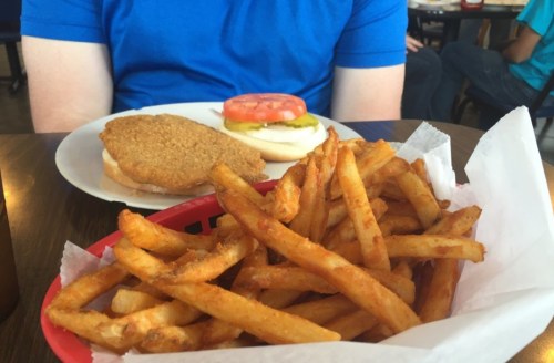 A plate with a sandwich and a slice of tomato, alongside a basket of golden, crispy fries.