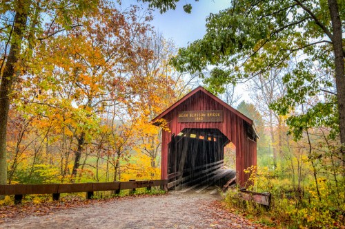A red covered bridge surrounded by vibrant autumn foliage and a misty atmosphere.