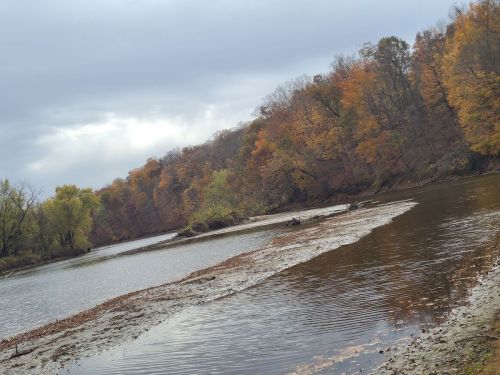 A serene river scene with autumn foliage along the banks, reflecting cloudy skies and gentle ripples on the water.