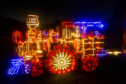 A vibrant display of illuminated pumpkins in various designs, glowing against a dark night sky.