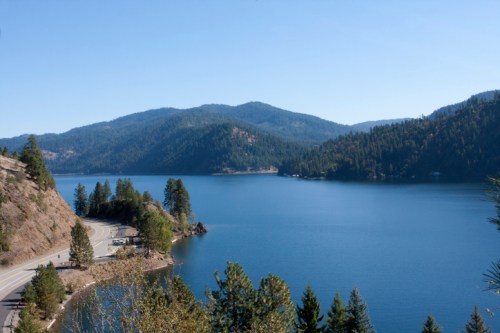 Scenic view of a calm lake surrounded by mountains and trees under a clear blue sky.