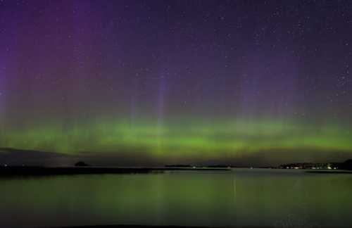 A stunning display of the aurora borealis over a calm lake, with vibrant green and purple hues against a starry sky.