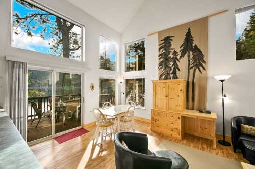 Bright, airy living space with large windows, wooden furniture, and a view of trees outside. Cozy dining area included.