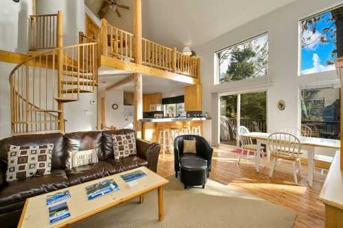 Bright, spacious living area with a spiral staircase, large windows, and cozy furniture in a modern cabin setting.