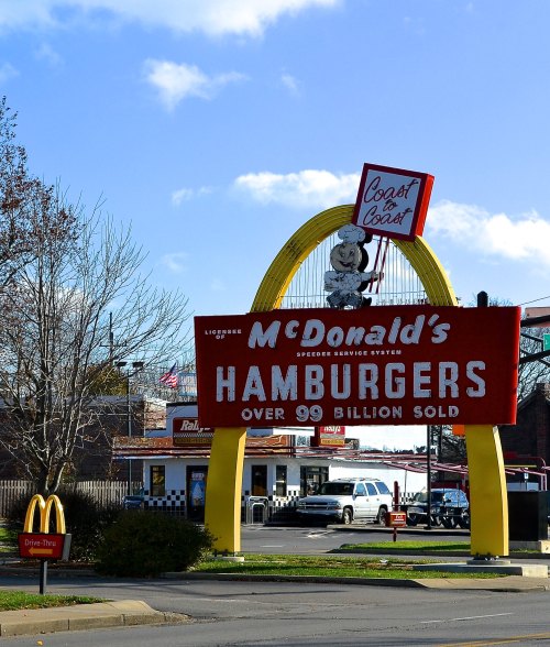 McDonald's sign featuring a large arch, cartoon character, and text about hamburgers sold, with a drive-thru below.