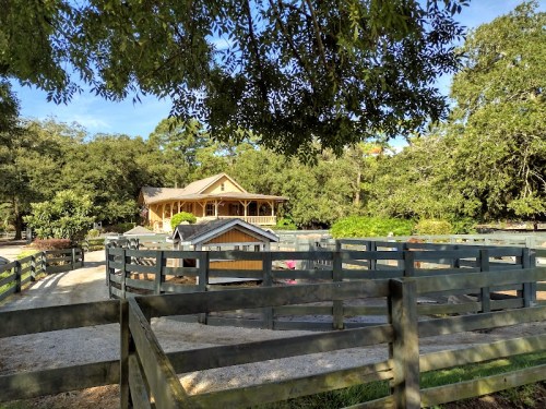 A wooden house surrounded by fenced areas and trees, set in a peaceful rural landscape.