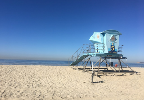 A blue lifeguard tower on a sandy beach with calm ocean waters and a clear blue sky.