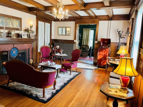 A cozy vintage living room with wooden beams, elegant furniture, and warm lighting, featuring a fireplace and decorative accents.