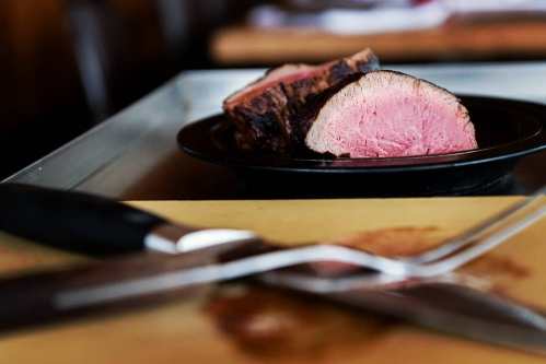 Sliced roast beef on a black plate, with a knife and carving fork in the foreground.