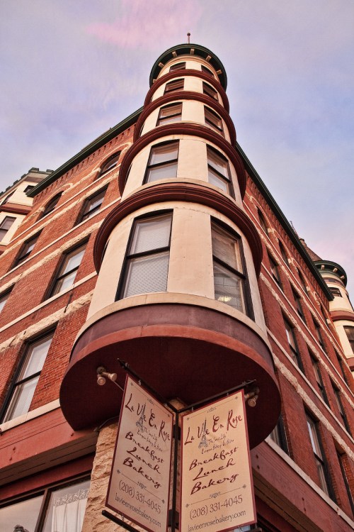 A low-angle view of a historic brick building with a rounded corner and signs for "La Vie En Rose Bakery."