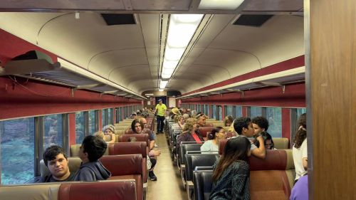 Interior of a train car filled with passengers seated in rows, some chatting and others looking out the windows.