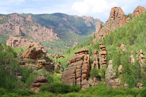 A scenic view of rocky formations surrounded by lush greenery and mountains under a partly cloudy sky.