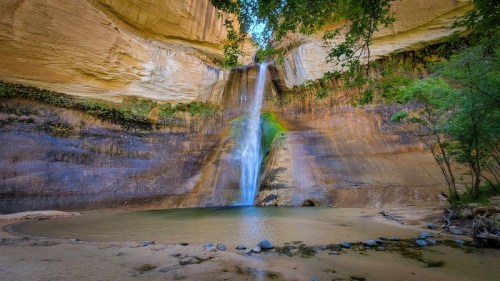 A serene waterfall cascades into a tranquil pool, surrounded by towering rock formations and lush greenery.