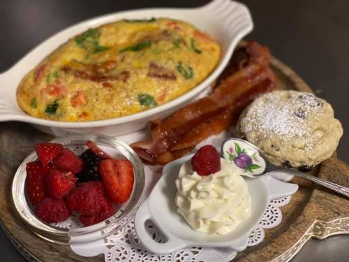 A plate featuring a vegetable frittata, crispy bacon, a scone with cream, and fresh berries.