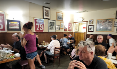 A busy restaurant scene with diners at tables, walls adorned with sports memorabilia and photos.