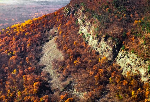 A scenic view of a rocky cliffside surrounded by vibrant autumn foliage in warm hues of orange and yellow.